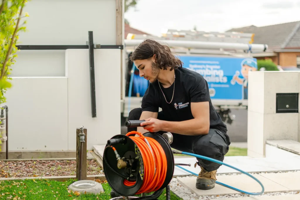 Plumber preparing drain inspection equipment beside a garden tap